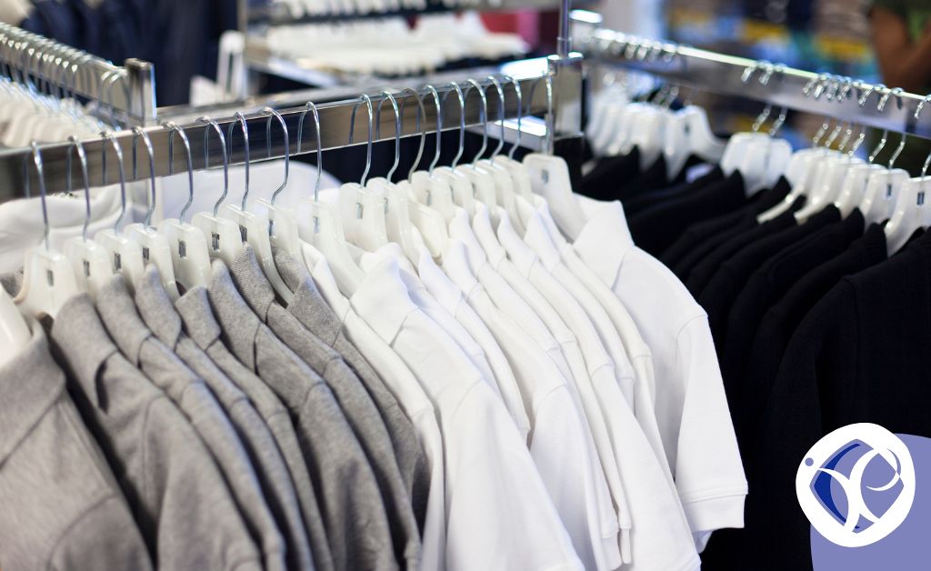 The image shows clothing rails in a shop, filled with grey, white and black shirts typical of many staff uniforms. It represents uniform allowance HMRC.