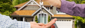 Image of a family member handing over the keys of a property to another family member. The property is in the background and out of focus.
